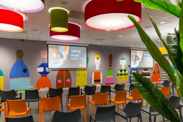 Kleurrijke vergaderruimte aan de Niels Bohrweg met stoelen, schermen en speelse muurillustraties.